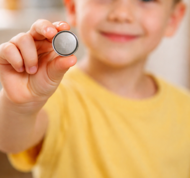 Kind mit Knopfbatterie in der Hand